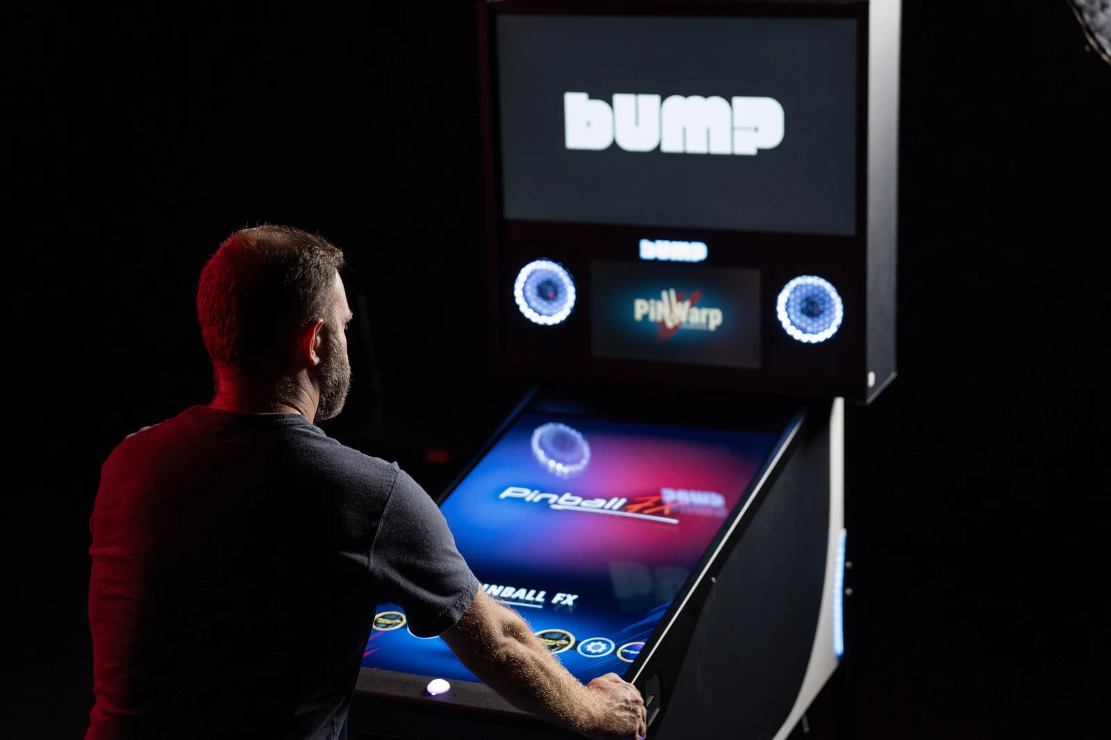 Jugador de pinball de espaldas ante un pinball digital BUMP, pantalla de inicio de Pinball FX en el tablero